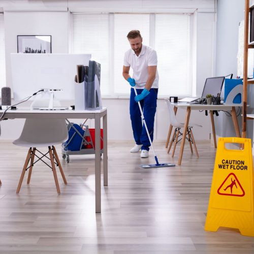 Male janitor with mop cleaning modern office floor